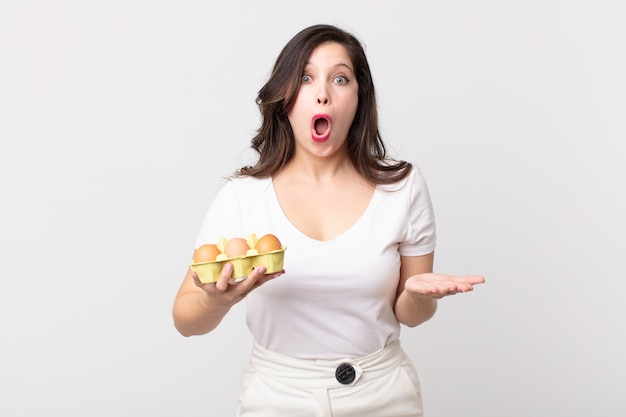 Pretty woman feeling extremely shocked and surprised and holding an eggs box