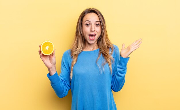 Pretty woman feeling happy and astonished at something unbelievable holding half orange