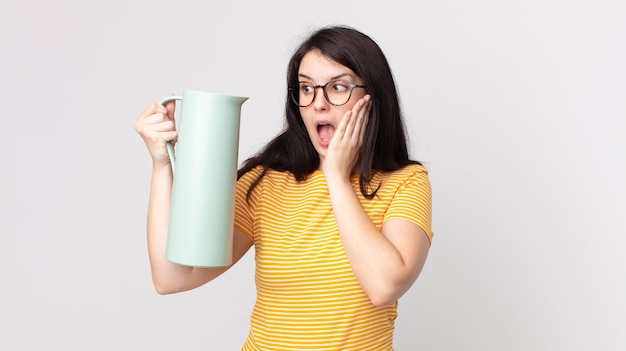 Pretty woman feeling happy, excited and surprised and holding a coffee thermos