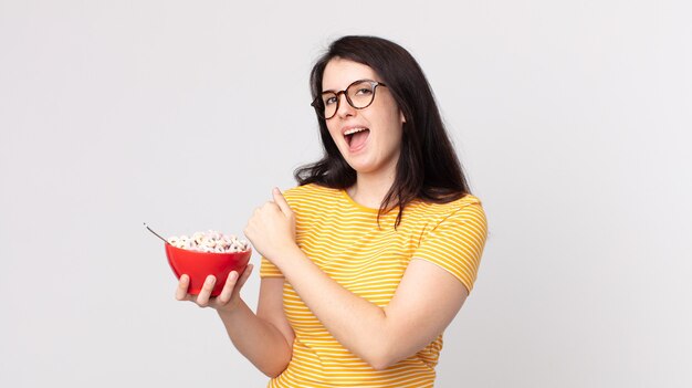 Bella donna che si sente felice e affronta una sfida o festeggia e tiene in mano una ciotola per la colazione