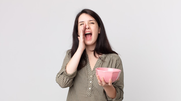 Bella donna che si sente felice, fa un grande grido con le mani vicino alla bocca che tiene una ciotola vuota. assistente agente con un auricolare