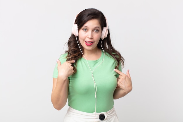 Pretty woman feeling happy and pointing to self with an excited listening music with headphones