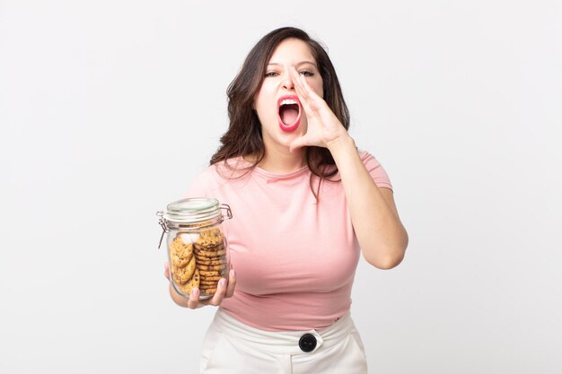 Pretty woman feeling happygiving a big shout out with hands next to mouth and holding a cookies glass bottle