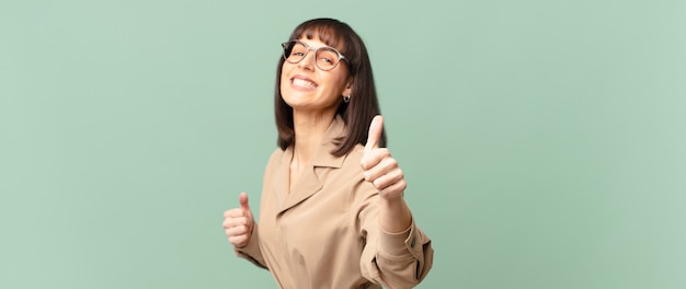 Foto bella donna che si sente orgogliosa, spensierata, sicura di sé e felice, sorride positivamente con il pollice in alto