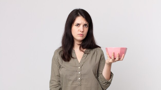 Foto bella donna che si sente triste, sconvolta o arrabbiata e guarda di lato con in mano una ciotola vuota. assistente agente con un auricolare