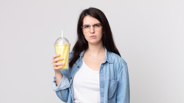 Pretty woman feeling sad, upset or angry and looking to the side and holding a vanilla milkshake