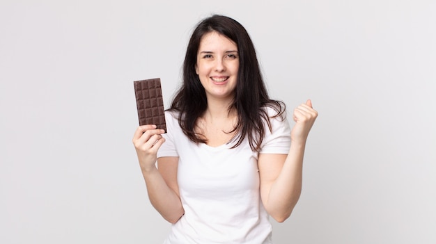 Bella donna che si sente scioccata, ride e celebra il successo e tiene in mano una barretta di cioccolato