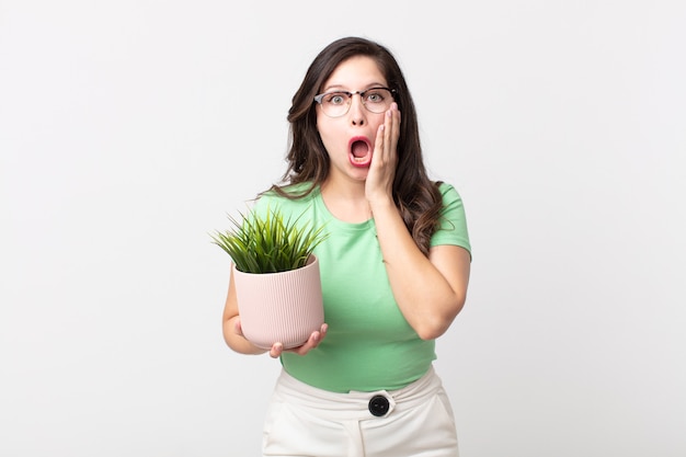 Pretty woman feeling shocked and scared and holding a decorative plant