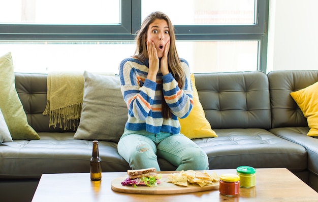 Photo pretty woman feeling shocked and scared, looking terrified with open mouth and hands on cheeks