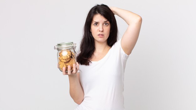 Pretty woman feeling stressed, anxious or scared, with hands on head and holding a cookies glass bottle