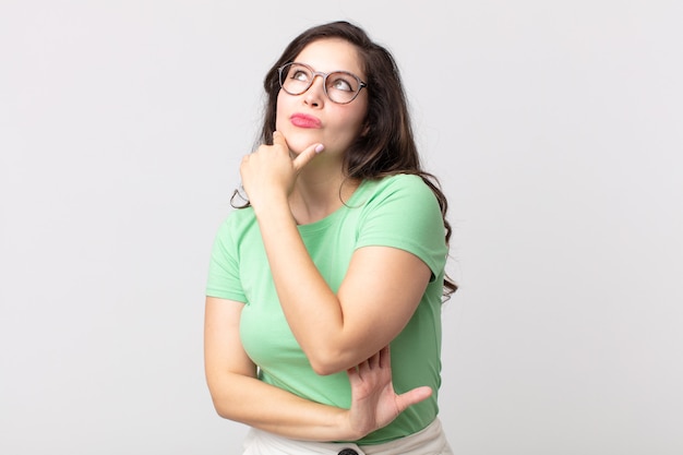 Foto bella donna che si sente premurosa, si chiede o immagina idee, sogna ad occhi aperti e alza lo sguardo per copiare lo spazio