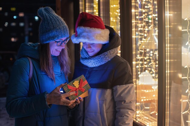 Pretty woman and her son in santas hat opening gift box on illuminated shop window