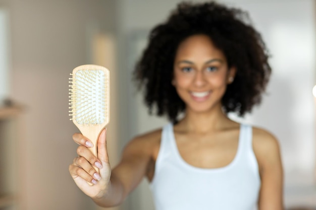 Pretty woman holding a big hairbrush, looking at the camera, making a white smile in the bathroom