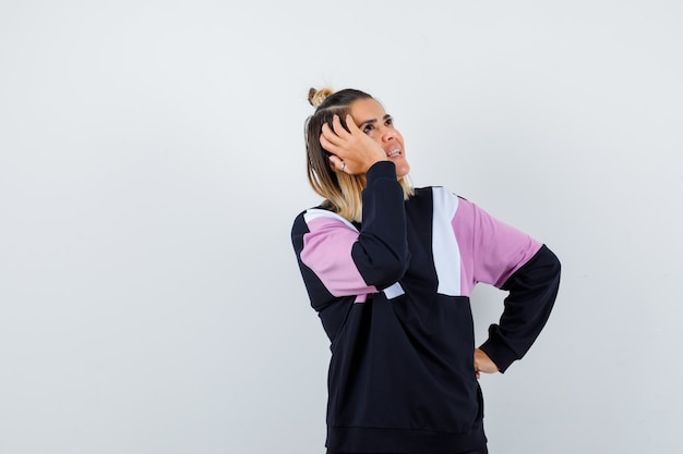 Pretty woman holding hand on head while looking up in sweatshirt and looking merry.