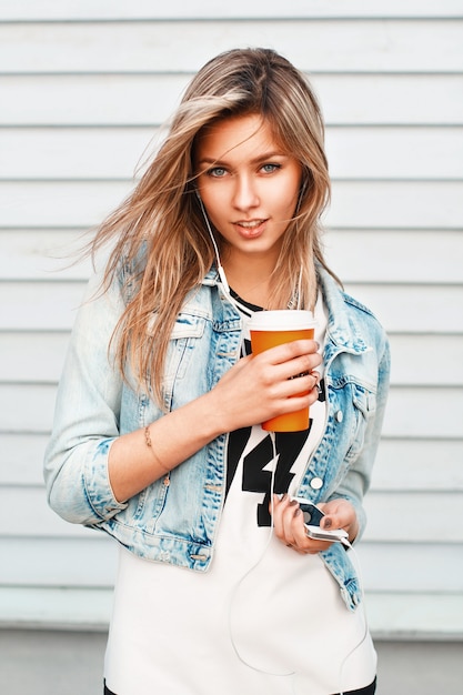 Pretty woman holding a paper cup of coffee and listening to music