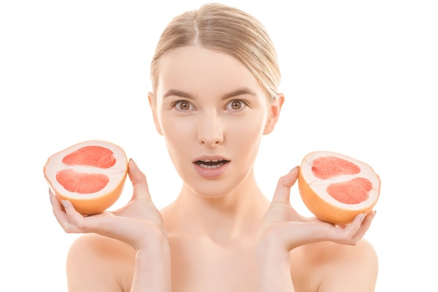 The pretty woman holding two halves of a grapefruit on the white background