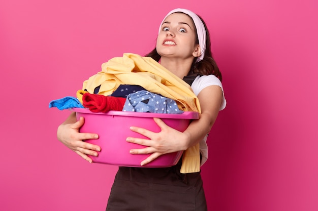 Pretty woman holds heavy basin with dirty clothes