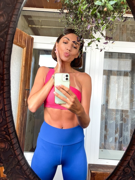 Pretty woman at home takes photo selfie in mirror on mobile phone for stories and posts in social media, wearing sport wear