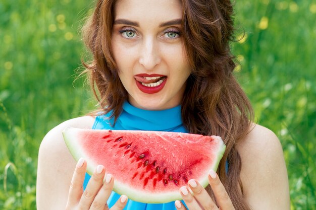 Pretty woman is holding slice of watermelon outdoors.