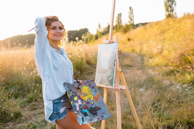 きれいな女性が絵を描いています。オープンエアセッション。かわいい女性は日没時に絵を描きます。ガールアーティスト