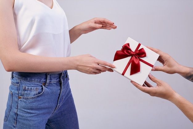 Bella donna è in piedi sul grigio con gli occhiali per pc e maglietta bianca. minuto di felicità. le mani di qualcun altro fanno un regalo, la donna è sorpresa.