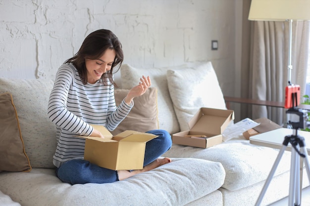 Pretty woman is unpacking parcel expressing joy sitting on sofa at home