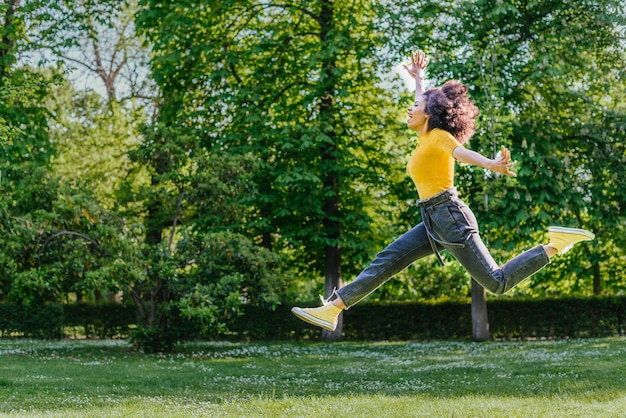 Pretty woman jumping happily in a garden. Side view. Full body.