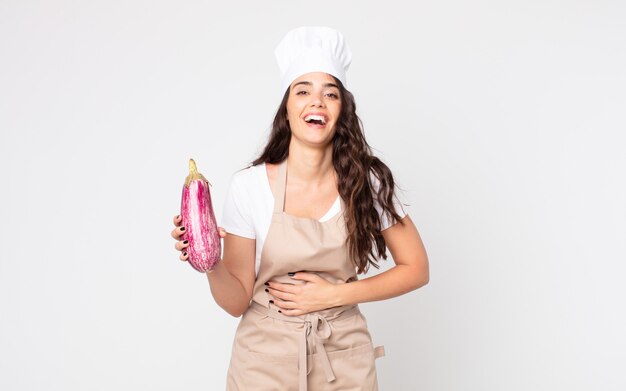 Pretty woman laughing out loud at some hilarious joke wearing an apron and holding an eggplant