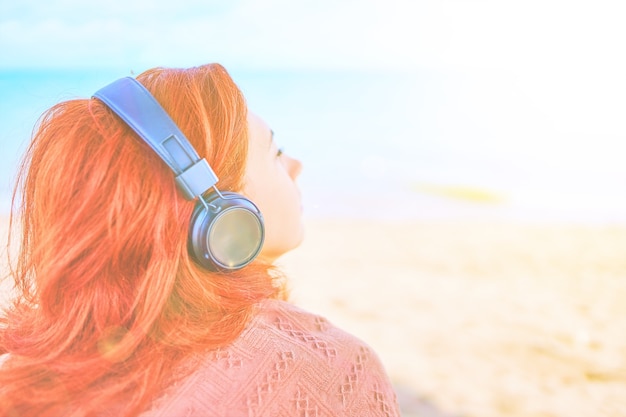 Pretty woman listening to music on the beach redhead girl listening to melody with listening device ...