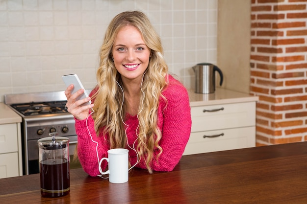 Pretty woman listening to music and having coffee in the kitchen