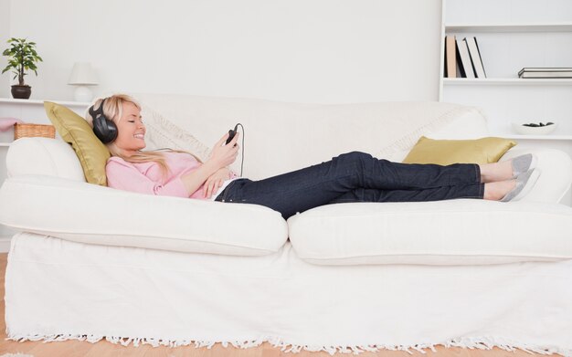 Pretty woman listening to music on her headphones while lying on a sofa