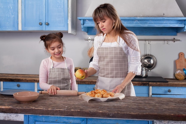 Pretty woman and little adorable daughter standing at table in kitchen cook together