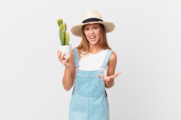 Pretty woman looking angry, annoyed and frustrated and holding a cactus decorative plant