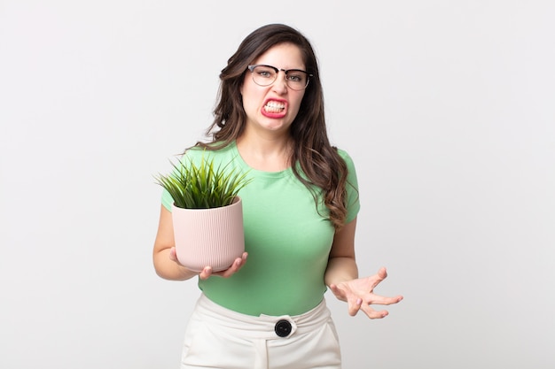 Pretty woman looking angry, annoyed and frustrated and holding a decorative plant