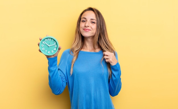 Pretty woman looking arrogant, successful, positive and proud holding an alarm clock