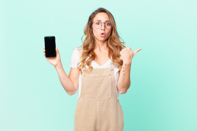 Pretty woman looking astonished in disbelief and holding a smartphone