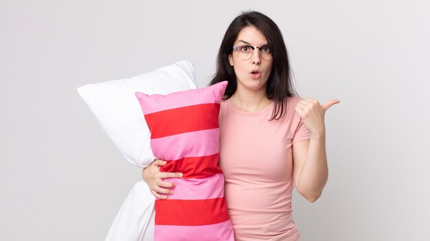 Pretty woman looking astonished in disbelief wearing pajamas and holding a pillow