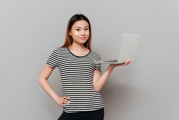 Donna graziosa che guarda macchina fotografica mentre tenendo computer portatile