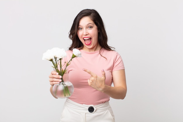 pretty woman looking excited and surprised pointing to the side and holding a decorative flowers pot