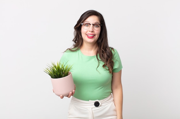 Pretty woman looking happy and pleasantly surprised and holding a decorative plant