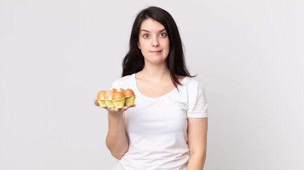 Pretty woman looking puzzled and confused and holding an eggs box