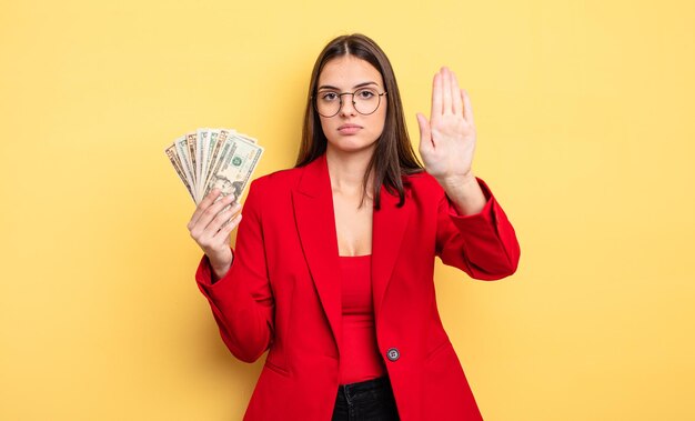 Foto donna graziosa che sembra seria mostrando il palmo aperto facendo il gesto di arresto del concetto di banconote in dollari