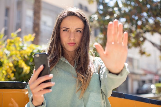 Foto bella donna che sembra seria mostrando il palmo aperto facendo il gesto di arresto del concetto di smartphone