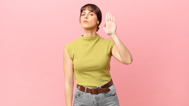 Pretty woman looking serious, stern, displeased and angry showing open palm making stop gesture