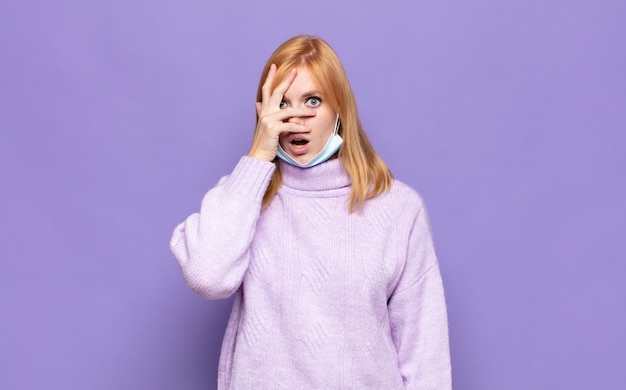 pretty woman  looking shocked, scared or terrified, covering face with hand and peeking between fingers