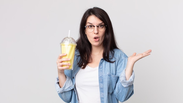 Pretty woman looking surprised and shocked, with jaw dropped holding an object and holding a vanilla milkshake