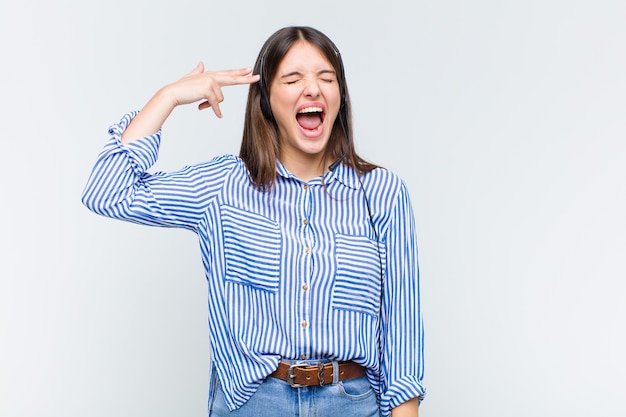 Pretty woman looking unhappy and stressed, suicide gesture making gun sign with hand, pointing to head