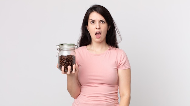 Foto donna graziosa che sembra molto scioccata o sorpresa e tiene in mano una bottiglia di chicchi di caffè