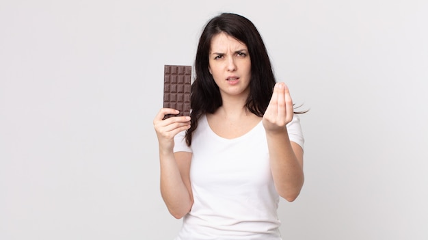 Pretty woman making capice or money gesture, telling you to pay and holding a chocolate bar