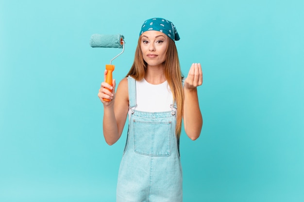 Pretty woman making capice or money gesture, telling you to pay painting a new home wall